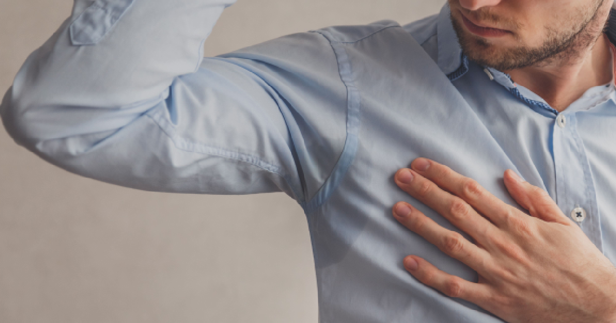 Man examining sweat stains on his shirt underarm representing Hyperhidrosis in Waterloo & Kitchener.
