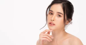 A woman with a neutral expression and a messy bun poses with her hand on her chin against a white background for Skin Booster in Waterloo & Kitchener.