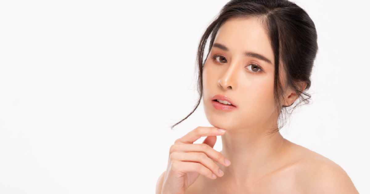 A woman with a neutral expression and a messy bun poses with her hand on her chin against a white background for Skin Booster in Waterloo & Kitchener.